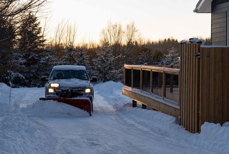 A plow-fitted pickup pushing snow off a driveway next to a freshly built deck and fence